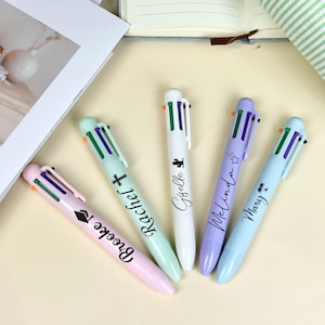 May include: Five multi-colour pens in pastel shades of pink, mint, white, lavender, and light blue. Each pen has a different name printed on it: Brooke, Rachel, Giselle, Melinda, and Mary. The pens are arranged on a light beige surface.