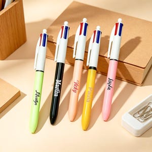 May include: Five multi-color retractable ballpoint pens with white clips and tops featuring red and blue accents. Each pen barrel is a different solid color: lime green, black, peach, yellow, and pink, with names printed in black script.