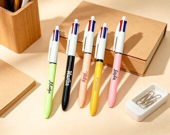 May include: Five multi-color retractable ballpoint pens with white clips and tops featuring red and blue accents. Each pen barrel is a different solid color: lime green, black, peach, yellow, and pink, with names printed in black script.