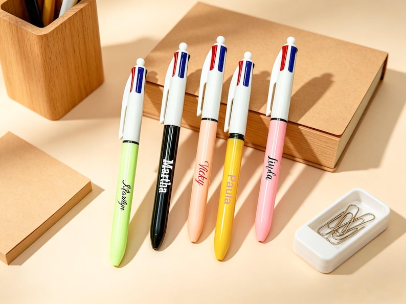 May include: Five multi-color retractable ballpoint pens with white clips and tops featuring red and blue accents. Each pen barrel is a different solid color: lime green, black, peach, yellow, and pink, with names printed in black script.