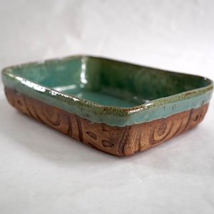 May include: A rectangular ceramic baking dish featuring a glossy teal glaze on the interior and upper rim. The exterior walls are made of unglazed, textured brown clay with carved swirl patterns wrapping around the sides of the vessel.