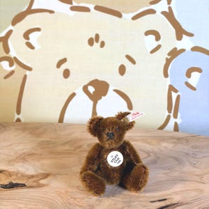 May include: A small, dark brown mohair teddy bear with a white Steiff Club 1999 chest tag and a signature Steiff button in its ear. The bear is seated in an upright position with articulated limbs and a stitched nose and mouth.