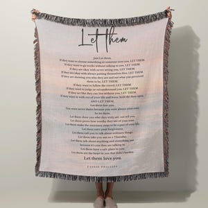 以下が含まれることがあります： 手書きフォントで「Let Them」という言葉が入った織りスローブランケット。ブランケットには同じタイトルの詩が掲載されています。ブランケットにはフリンジエッジと背景に風景デザインがあります。