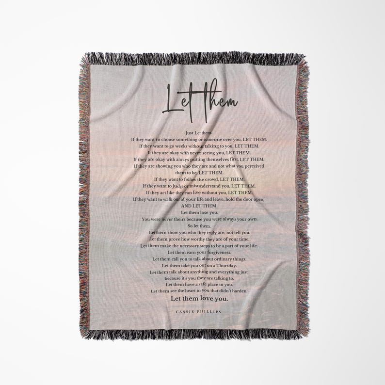 以下が含まれることがあります： フリンジ付きの縁取りが施された、クリーム色のスローブランケット。「Let Them」の文字がスタイリッシュなフォントで表示され、詩が添えられています。詩のテキストは、暗くエレガントなフォントです。