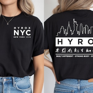 May include: Black t-shirt with white text. The front features "HYROX NYC NEW YORK 2026". The back displays a New York City skyline graphic above "HYROX" and fitness icons. Text below reads "BUILT DIFFERENT - STRONG BODY - STRONG MIND".