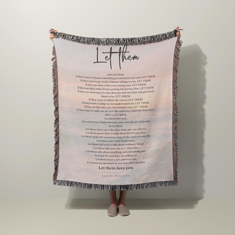 以下が含まれることがあります： 手書きフォントで「Let Them」という言葉が入った織りスローブランケット。ブランケットには同じタイトルの詩が掲載されています。ブランケットにはフリンジエッジと背景に風景デザインがあります。