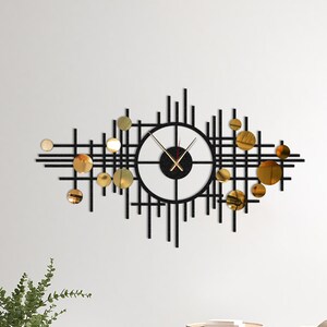 May include: A black and gold geometric wall clock with a circular clock face and gold accents. The clock is mounted on a white wall in a living room setting.