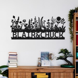 Op de afbeelding: Zwarte metalen wandkunst met een silhouet van een tuin met de namen Blair & Chuck.