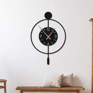May include: A black modern wall clock with a round face and a pendulum. The clock has a black metal frame and a white background with black numbers. The clock is hanging on a white wall.