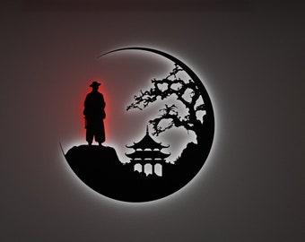 Könnte beinhalten: Schwarze Wandkunst mit einer Silhouette einer Figur mit Hut, die auf einem Felsen steht, mit einer Pagode und einem Baum in einer Halbmondform. Die Figur hat einen roten Schein. Die Kunst ist an einer grauen Wand befestigt.