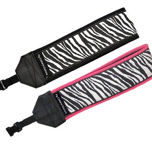 May include: Two camera straps with a zebra print design. One strap has a black border and the other has a pink border. Both straps have the text "My Camera Couture" printed on them.