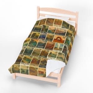 May include: A twin-sized bed with a blanket featuring vintage-style illustrations of U.S. National Parks. The blanket showcases various parks with their names and numbers, including Everglades, Yosemite, and Grand Canyon. The color palette includes shades of brown, beige, and green.