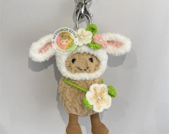 Puede incluir: Llavero de oveja de peluche con un disfraz de cordero blanco y crema. La oveja lleva una corona de flores y sostiene una flor. El llavero tiene un cierre y un anillo plateados. El texto "NEIGHBOR GIRLS" está en la cabeza de la oveja.