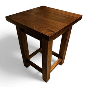 Puede incluir: Un taburete de madera marrón oscuro con una parte superior cuadrada y un marco simple y robusto.