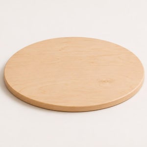 May include: A circular wooden board with a smooth, light tan surface and visible natural wood grain patterns. The object features a flat top and rounded edges, presenting a simple, uniform, and solid construction made from light-colored timber.