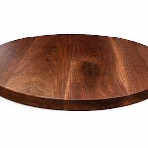 May include: A round, solid wood tabletop with a rich, dark brown finish. The wood grain is visible, adding texture and character to the surface. The tabletop is ideal for a dining table or a decorative piece.