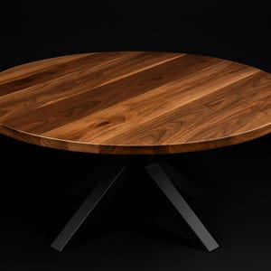 May include: A round wooden table with a dark walnut finish. The tabletop is supported by a black metal base with angled legs. The table is set against a black background, highlighting its modern design.