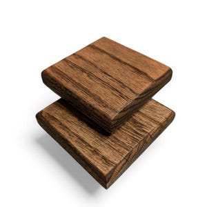 Puede incluir: Dos posavasos de madera apilados uno encima del otro. Los posavasos son de color marrón oscuro con un patrón de veta de madera.