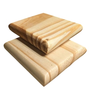 May include: Two square wooden coasters with rounded edges. The coasters are made of light-colored wood with visible grain patterns. One coaster is stacked on top of the other, showcasing the natural wood tones and design.