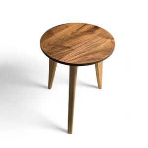 Könnte beinhalten: Ein runder Holz-Beistelltisch mit naturbelassenem Holzfinish und drei Beinen. Die Tischplatte ist aus Walnussholz.