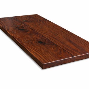 May include: A rectangular, solid wood tabletop with a rich, dark brown finish. The wood grain is prominent, featuring swirling patterns and knots. The edges are clean and squared, suggesting a modern design. The tabletop is ideal for a desk or table.