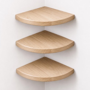 May include: Three light-toned wood corner shelves mounted in a vertical stack. Each shelf features a quarter-circle shape with a curved front edge and a visible natural wood grain pattern, designed to fit flush into the corner of a room.
