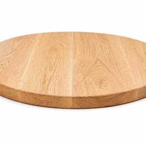 Könnte beinhalten: Ein rundes Schneidebrett aus hellem Holz mit sichtbarer Holzmaserung. Das Brett besteht aus massivem Holz und hat eine glatte, fertige Oberfläche. Die Kanten sind abgerundet. Ideal für die Zubereitung von Speisen.