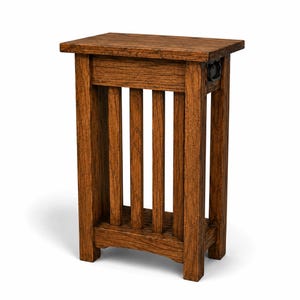 Könnte beinhalten: Ein Beistelltisch im Craftsman-Stil aus gebeiztem Holz. Der Tisch hat eine rechteckige Oberseite, vertikale Lamellen und ein kleines Regal. Ein dunkler Metallring befindet sich an der Seite. Der Tisch ist etwa 61 cm hoch.