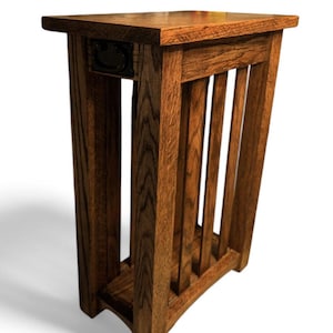 Puede incluir: Una mesa auxiliar de madera marrón oscuro con un solo estante y una manija de metal decorativa. La mesa tiene un diseño simple y tradicional.