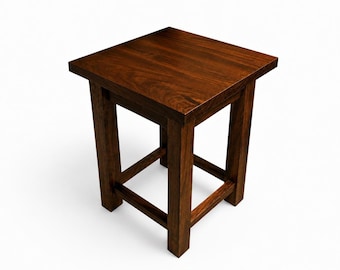 Può includere: Un piccolo sgabello quadrato in legno con finitura marrone scuro. Lo sgabello ha un design semplice con quattro gambe e un piano piatto. Le gambe sono collegate da un telaio inferiore per una maggiore stabilità. L'altezza è di circa 46 cm.