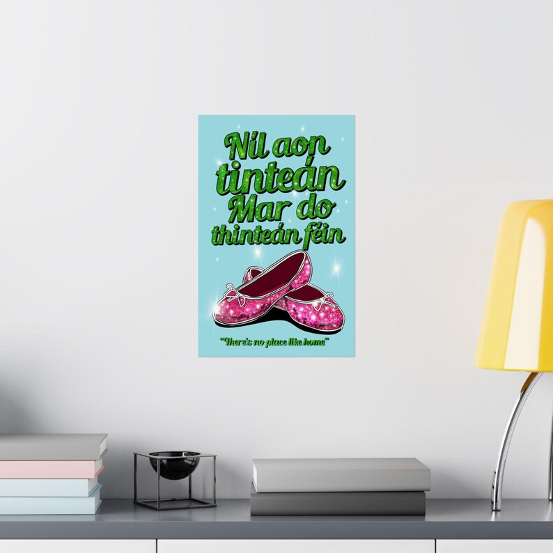 K&ouml;nnte beinhalten: Ein blaues und gr&uuml;nes Poster mit dem Text "Nil aon tintean mar do thintean fein" in gr&uuml;nem Glitzer. Der Text wird mit "Es gibt keinen Ort wie zu Hause" &uuml;bersetzt. Das Poster zeigt ein Paar rosa glitzernde Schuhe.