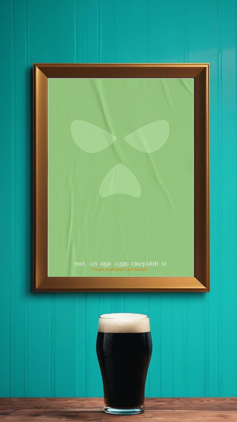 Peut inclure: Une affiche verte encadr&eacute;e avec un design de visage stylis&eacute; et du texte en ga&eacute;lique, au-dessus d'une pinte de stout fonc&eacute;. L'affiche est dans un cadre marron, sur un mur turquoise. La stout a une t&ecirc;te &eacute;paisse et cr&eacute;meuse.