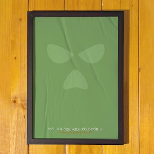 Peut inclure: Affiche encadr&eacute;e avec un fond vert et un design de visage stylis&eacute;. L'affiche porte le texte "mol an &oacute;ige agus tiocfaidh si" et "Praise youth and it will flourish". Le cadre est noir, et le fond est un mur en bois.