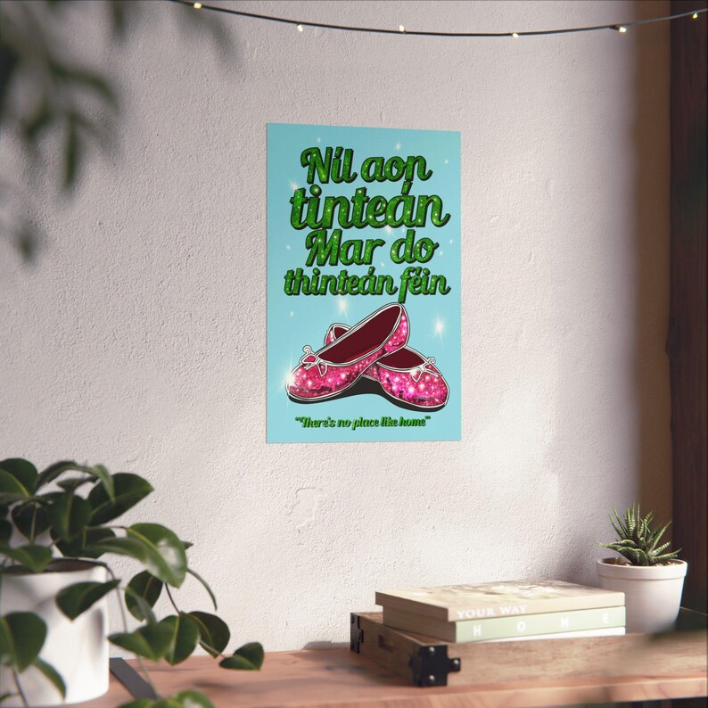 K&ouml;nnte beinhalten: Ein Poster mit hellblauem Hintergrund, auf dem ein Paar rosa glitzernde Schuhe und der Text in Gr&uuml;n zu sehen ist: "Nil aon tintean Mar do thintean f&eacute;in" und "There's no place like home".