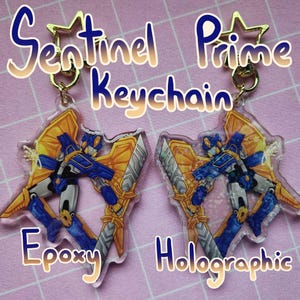 May include: Two Sentinel Prime keychains, one with a holographic finish and one with an epoxy finish. Both keychains feature a blue and gold robot with wings.