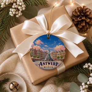 May include: A round ceramic ornament featuring a colorful illustration of the Grote Markt in Antwerp, Belgium, with the Brabo Fountain in the center. The text ANTWERP BELGIUM is printed in dark blue at the bottom of the ornament.