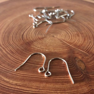 May include: Two silver earring hooks on a wooden surface. The hooks are made of metal and have a simple design.
