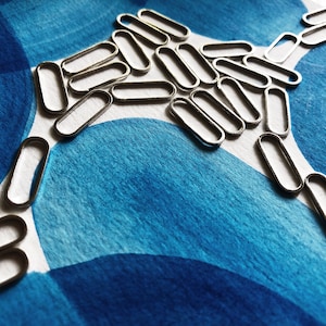 May include: A collection of silver-colored, oval-shaped metal findings arranged on a blue and white patterned surface. The findings are evenly spaced, creating a visual pattern against the textured background.