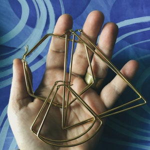 Könnte beinhalten: Ein Set aus drei goldenen geometrischen Ohrringen, bestehend aus einem Hexagon, einem Dreieck und einem Halbkreis. Die Ohrringe sind übereinander gelegt.