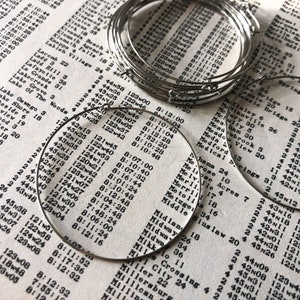 May include: A close-up of a stack of silver hoop earrings. The earrings are arranged in a circular pattern, with the largest hoop at the bottom and the smallest hoop at the top. The hoops are all made of a smooth, shiny metal.