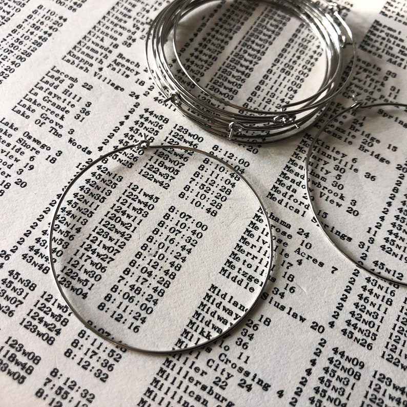 May include: A close-up of a stack of silver hoop earrings. The earrings are arranged in a circular pattern, with the largest hoop at the bottom and the smallest hoop at the top. The hoops are all made of a smooth, shiny metal.