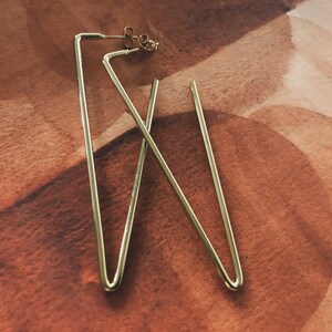 May include: A pair of gold triangle shaped earrings. The earrings are made of thin metal and have a simple design.