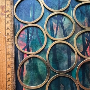 May include: A set of brass coasters with a circular shape. The coasters are arranged in a pattern on a blue and green background with abstract brushstrokes.