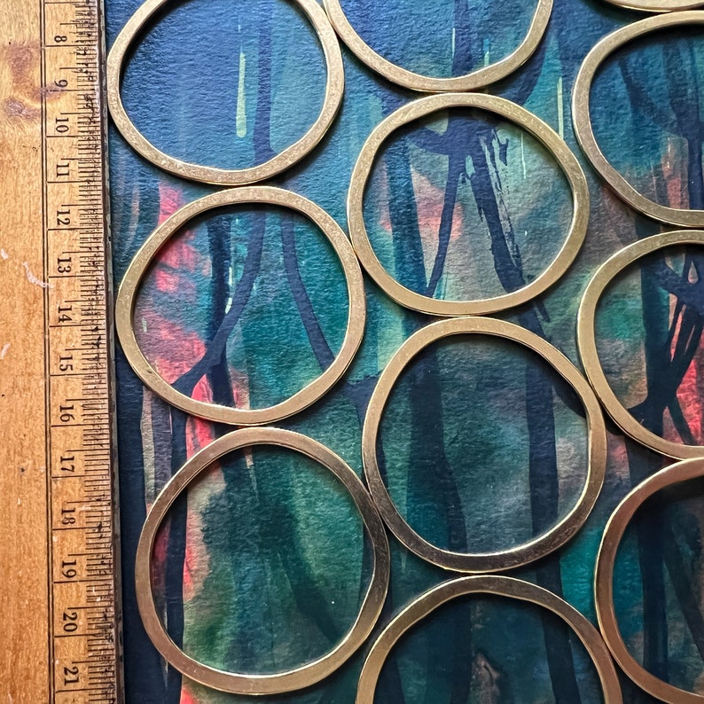May include: A set of brass coasters with a circular shape. The coasters are arranged in a pattern on a blue and green background with abstract brushstrokes.