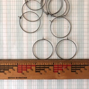 May include: A set of ten silver-colored metal hoops, measuring approximately 7 inches in diameter, are arranged on a gridded surface. A wooden ruler with markings in inches is placed below the hoops.