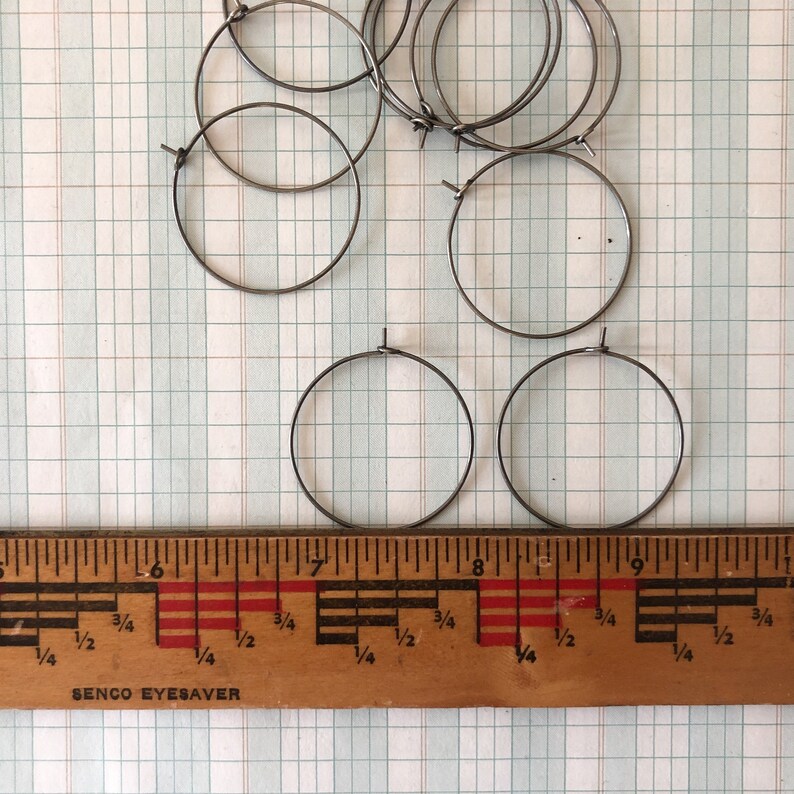 May include: A set of ten silver-colored metal hoops, measuring approximately 7 inches in diameter, are arranged on a gridded surface. A wooden ruler with markings in inches is placed below the hoops.