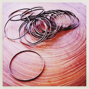 May include: A pile of thin, silver-colored metal rings on a wooden surface with a reddish-brown grain.