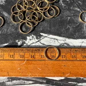 Puede incluir: Un primer plano de una regla de metal dorado con los números del 11 al 19 marcados en ella. Un solo anillo de metal dorado se coloca en la regla entre los números 15 y 16. El anillo tiene un diámetro de aproximadamente 3,8 cm.