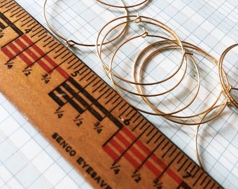 May include: A set of five gold hoop earrings of varying sizes, measured against a wooden ruler with the text "SENCO EYESAVER".