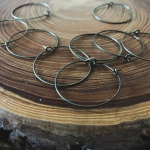 May include: A set of six silver hoop earrings on a wooden surface. The hoops are all the same size and are arranged in a random pattern.